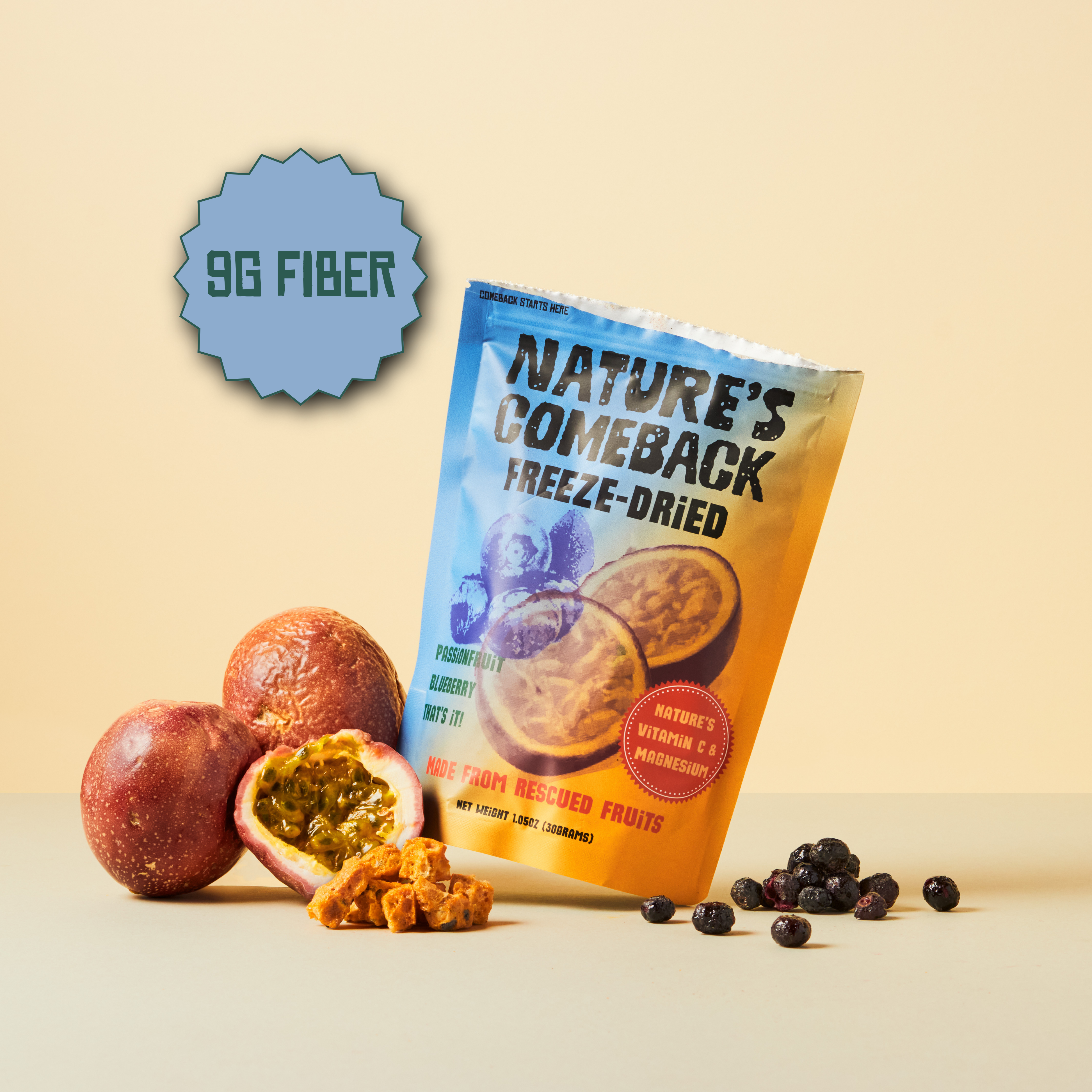 A stand-up pouch of Nature's Comeback Freeze-Dried fruit snacks is displayed on a beige surface with whole and halved passion fruit, loose dried fruit pieces, and dark berries around it. A blue badge in the upper left reads '9G FIBER'.